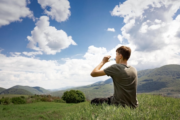 Le gars est assis sur une montagne et boit de l'eau d'un paysage de montagne en bouteille