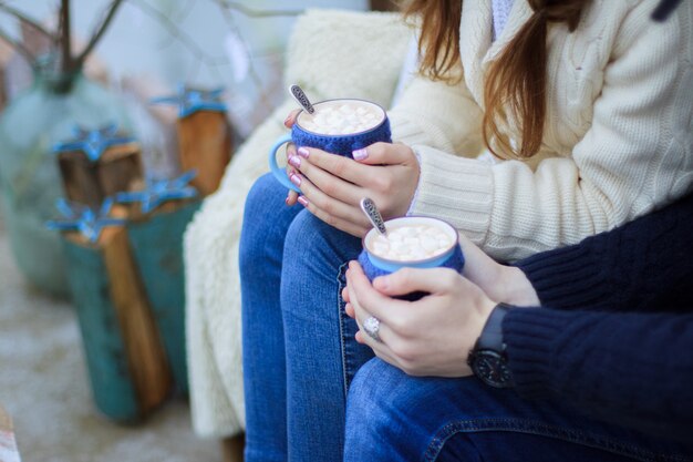 Un gars et une fille en jean bleu tiennent des tasses bleues de cacao dans leurs mains.