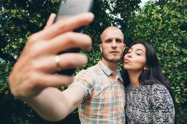 Un gars avec une fille prenant des selfies sur un feuillage vert.