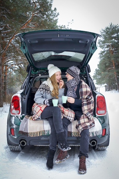 un gars et une fille sont assis dans le coffre d'une voiture, dans une couverture avec une tasse de thé