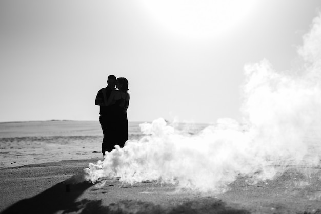 Un gars et une fille en vêtements noirs s'embrassent à l'intérieur d'une fumée blanche