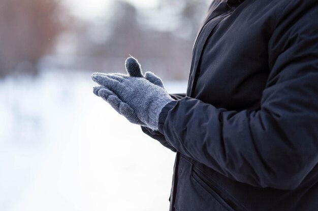 Le gars en gants se réchauffe les mains Le gars se réchauffe les mains Mains en gants d'hiver gris La paume avec le gant dans la neige