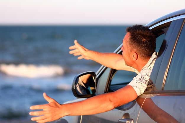 Un gars heureux dans la voiture au bord de la mer dans la nature en voyage de vacances