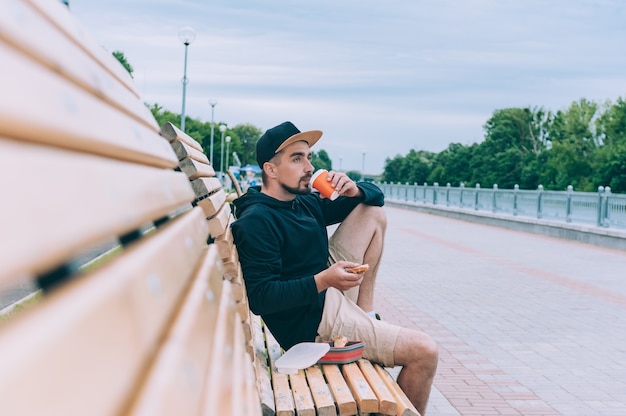 Un gars hipster était assis sur un banc et en train de dîner