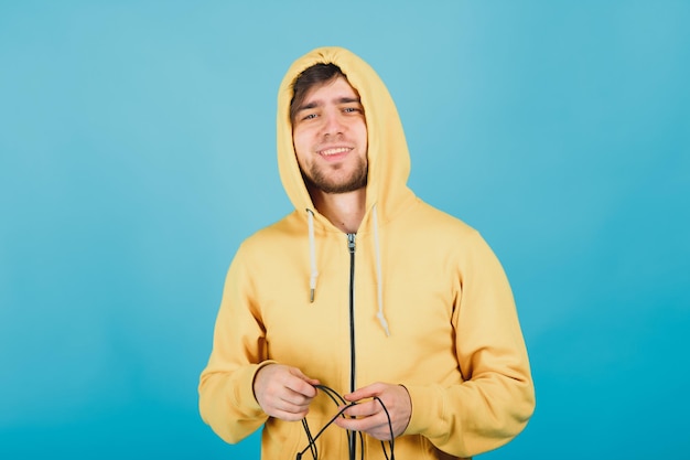 un gars joyeux dans un sweat à capuche jaune regarde la caméra et sourit sur un fond bleu