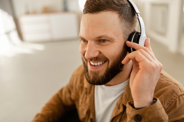 Un gars joyeux qui écoute de la musique en ligne avec des écouteurs à la maison