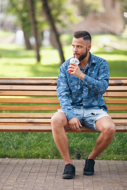 gars avec de la limonade se repose dans un parc sur un banc au printemps. Journée ensoleillée.