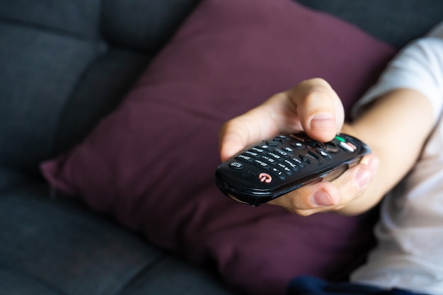 Photo un gars maigre dans les vêtements de la maison est assis sur un canapé et regarde la télévision. mec ennuyé avec télécommande tv