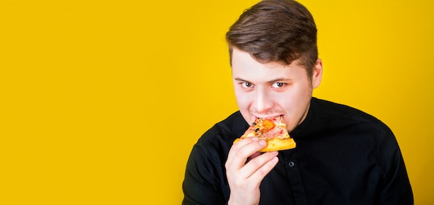 Le gars mange de la pizza sur un espace jaune et sourit.