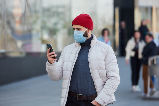 Un gars avec un masque sur le visage à l'aide d'un smartphone dans le centre de la ville.