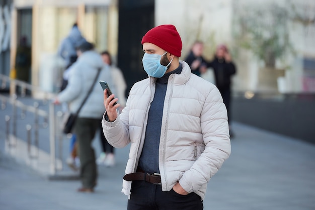 Un gars avec un masque sur le visage à l'aide d'un smartphone dans le centre de la ville.