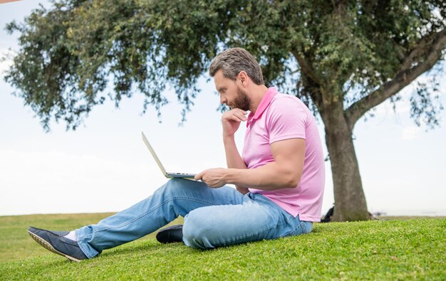 Un gars occupé vérifie ses e-mails sur un ordinateur relaxant sur l'éducation en ligne sur l'herbe