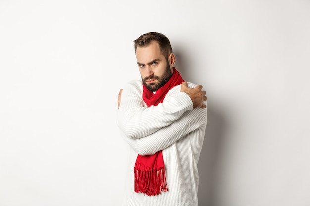 Un gars offensé s'embrassant et ayant l'air mécontent de la caméra, boudant en se tenant debout sur fond blanc