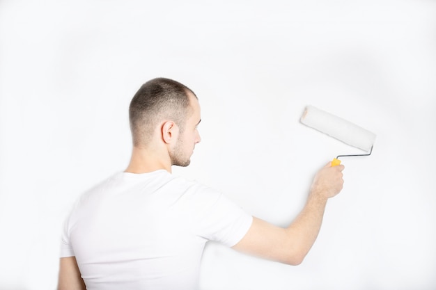 Le gars peint le mur avec un rouleau de construction.