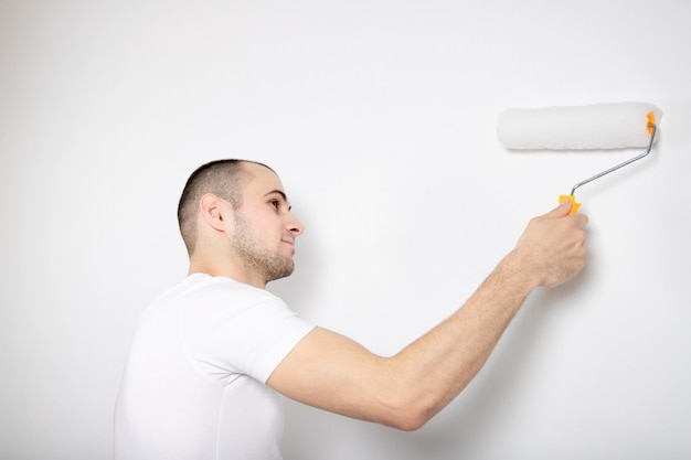 Le gars peint le mur avec un rouleau de construction.