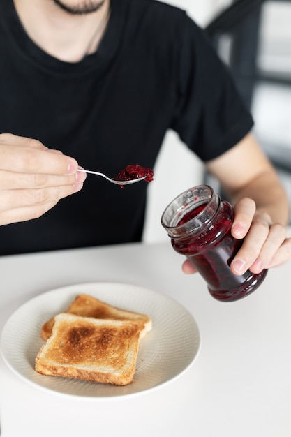 Le gars prend le petit déjeuner avec du pain grillé avec de la confiture.