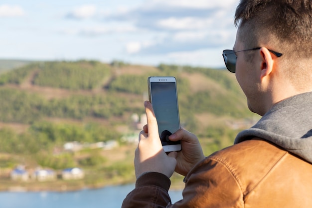 Le gars prend une photo au téléphone debout sur les rives de la rivière