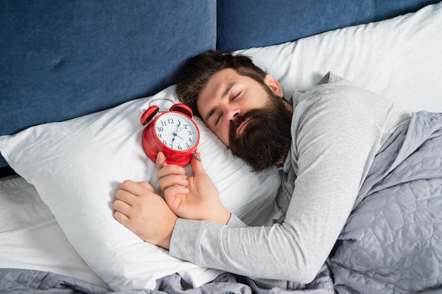 Un gars qui dort avec un réveil au lit