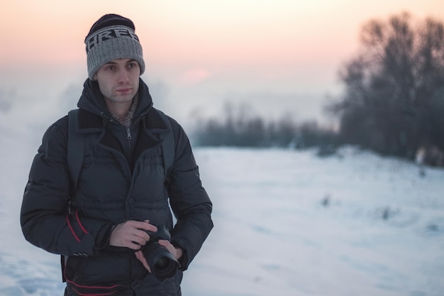 Un gars se tient avec un appareil photo en hiver, sur le côté gauche du cadre pour le texte