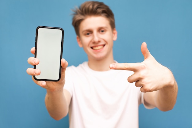 Un gars souriant pointe son doigt sur un smartphone avec un écran blanc.