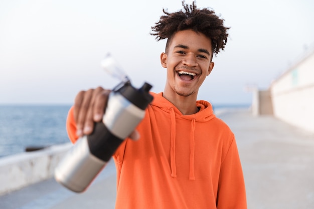 Photo gars de sport à l'extérieur sur la plage d'eau potable tenant une bouteille