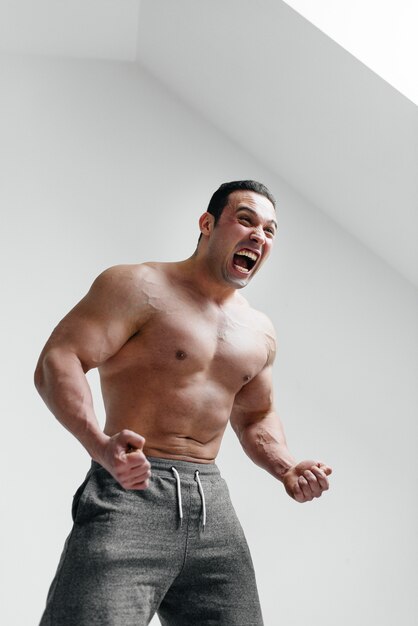 Un gars sportif hurle de rage contre un mur blanc. Colère. Menace.