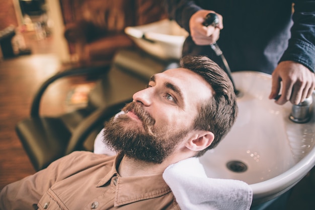 Un gars sympa prend soin de ses cheveux. Le coiffeur se lave les cheveux. Le client est détendu et heureux.