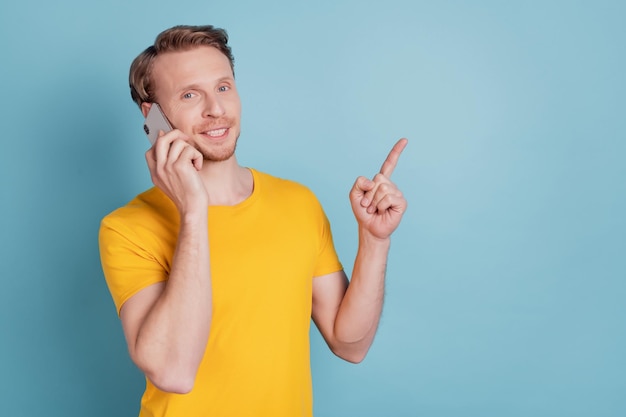 Un gars sympathique tient une conversation téléphonique avec un doigt direct dans l'espace vide porte des vêtements décontractés isolés sur fond turquoise