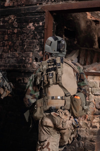 un gars en uniforme militaire se tient le dos dans le contexte d'un vieux mur dans un dilapida