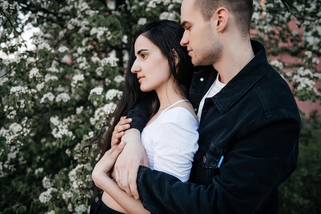 Un gars en vêtements noirs a étreint une fille dans un t-shirt blanc sur fond de fleurs de jasmin