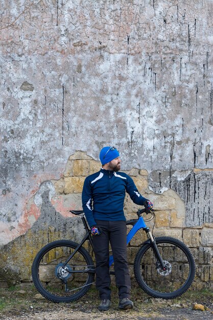 Un gars en vêtements de sport montant des vêtements sur un vélo de montagne sur un mur de béton de brique vintage