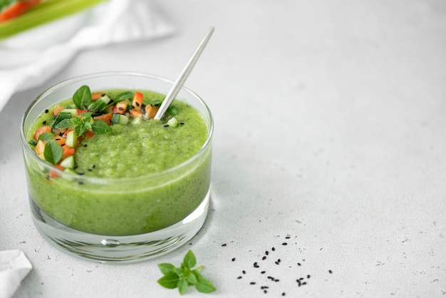 Gaspacho de concombre réfrigéré avec des morceaux de tomate et du basilic dans un bol en verre gros plan de l'espace de copie