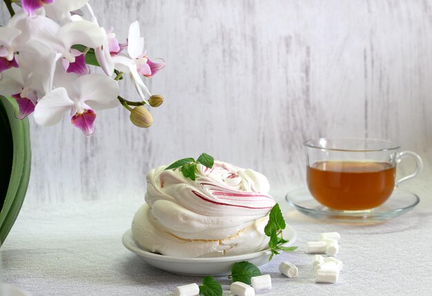 gâteau aéré à la meringue sur fond clair et une tasse de thé encadrée par une orchidée blanche en fleurs