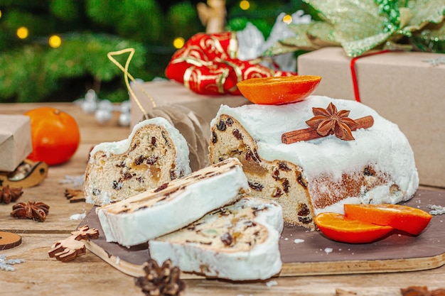 Gâteau allemand traditionnel de Noël Stollen Pâtisserie européenne parfumée pain cuit à la maison avec des épices et des fruits secs Branches d'arbres de Noël et décorations fond en bois gros plan