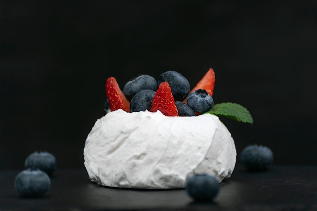 Gâteau Anna Pavlova sur fond noir. Gâteau meringué à l'air avec des fraises fraîches et des myrtilles.