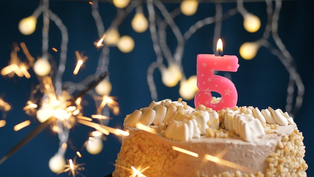 Gâteau d'anniversaire avec 5 bougies roses et cierge magique brûlant sur fond bleu. Fermer