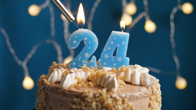 Gâteau d'anniversaire avec bougie à 24 chiffres sur fond bleu incendié par un briquet. Fermer