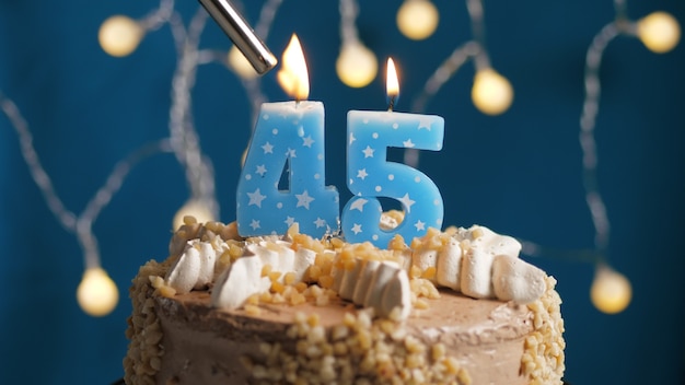 Gâteau d'anniversaire avec une bougie à 45 chiffres sur fond bleu incendié par un briquet. Fermer
