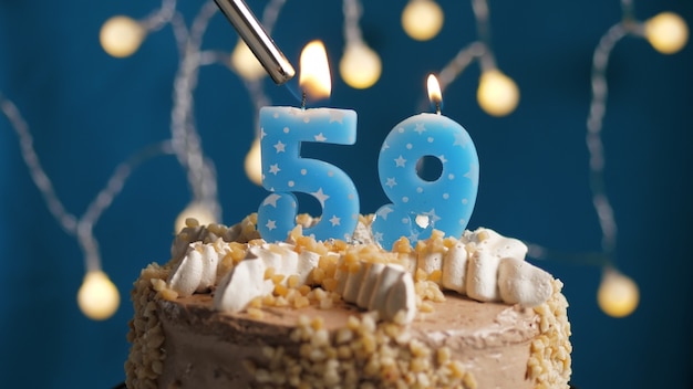 Photo gâteau d'anniversaire avec bougie numéro 59 sur fond bleu incendié par un briquet. fermer