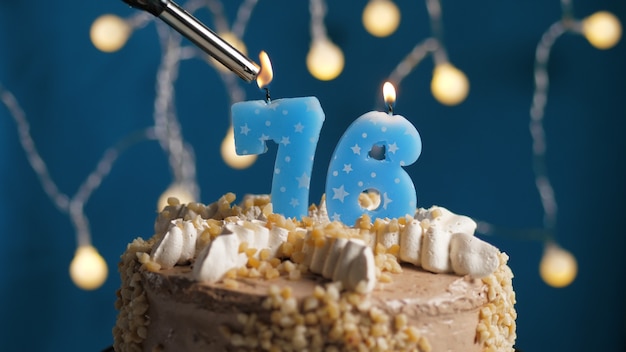 Gâteau d'anniversaire avec bougie numéro 76 sur fond bleu incendié par un briquet. Fermer