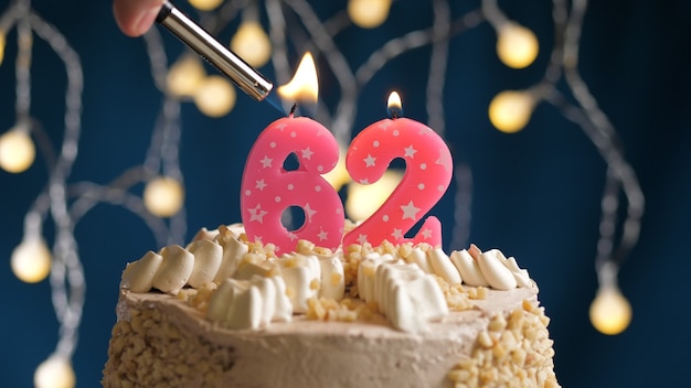 Gâteau d'anniversaire avec bougie rose numéro 62 sur fond bleu incendié par un briquet. Vue rapprochée
