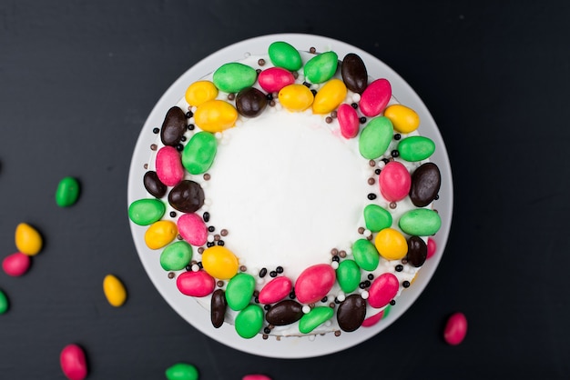 Gâteau d'anniversaire avec décor crème et bonbons sur une surface noire