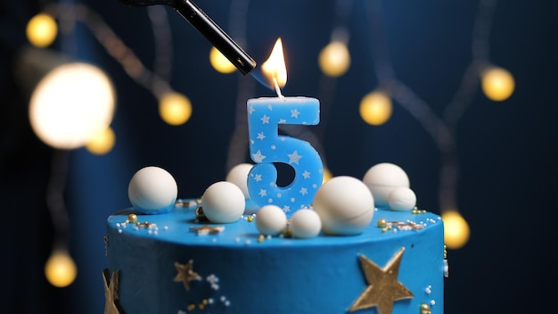 Gâteau d'anniversaire numéro 5 étoiles ciel et concept de lune, la bougie bleue est allumée par un briquet. Copiez l'espace sur le côté droit de l'écran. Fermer