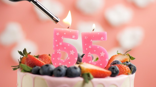 Gâteau d'anniversaire numéro 55 bougie rose sur beau gâteau aux baies et briquet avec feu sur fond de nuages blancs et ciel rose Vue rapprochée