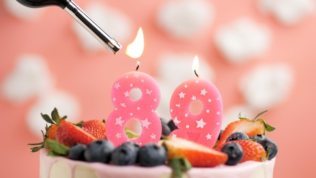 Gâteau d'anniversaire numéro 89 bougie rose sur beau gâteau aux baies et briquet avec feu sur fond de nuages blancs et ciel rose Vue rapprochée