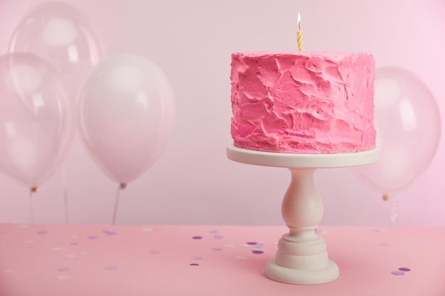 Gâteau d'anniversaire sucré et savoureux avec une bougie allumée sur un présentoir à gâteaux près de ballons à air et décoration sur