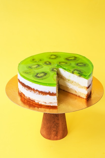 Gâteau d'anniversaire tranché décoré de gelée verte et de kiwi sur le support à gâteau en bois. Belle génoise à la crème fouettée. Fond jaune. Espace de copie. Photographie culinaire pour la recette.