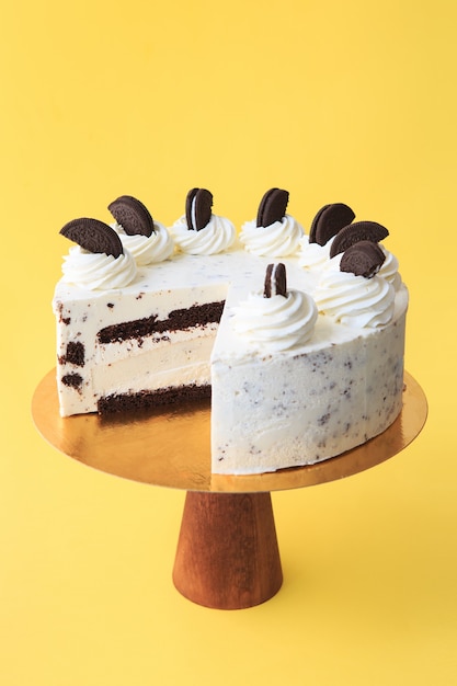 Gâteau d'anniversaire en tranches sur le stand de gâteau en bois. Beau gâteau blanc à la crème fouettée décoré de biscuits au chocolat noir. Fond jaune. Espace de copie. Photographie culinaire pour la recette.
