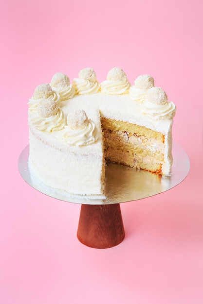 Gâteau d'anniversaire en tranches sur le stand de gâteau en bois. Belle génoise blanche à la crème fouettée. Fond rose. Espace de copie. Photographie culinaire pour la recette.