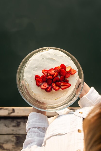 Gâteau appétissant décoré de fraises dans des mains féminines sur le fond de la rivière